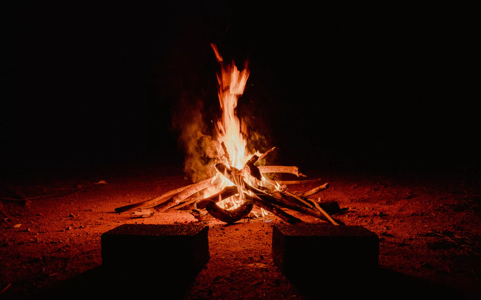 A red-coloured campfire on the ground during a dark night.