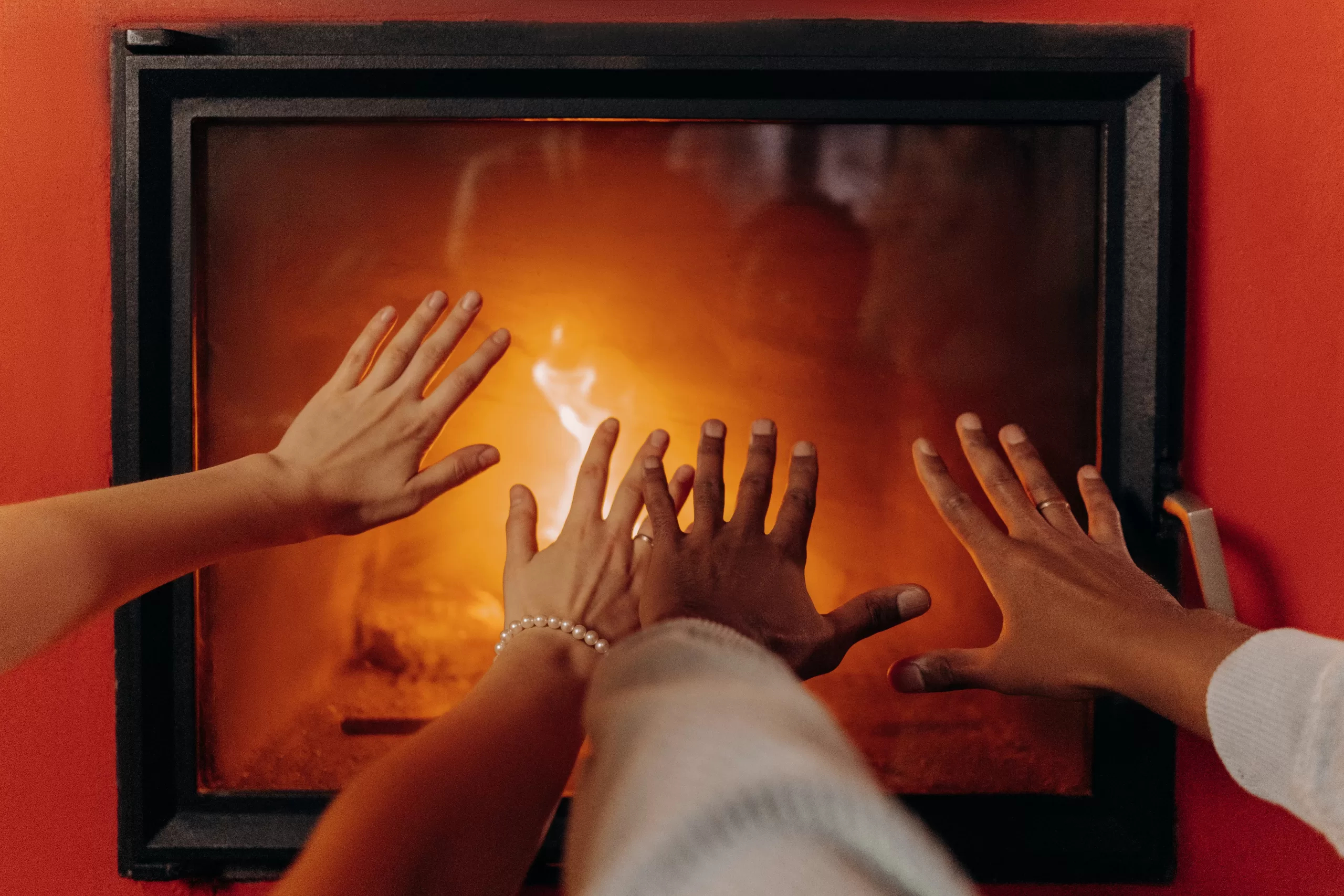 A man and a women hands reaching for the warmth of an enclosed fireplace.